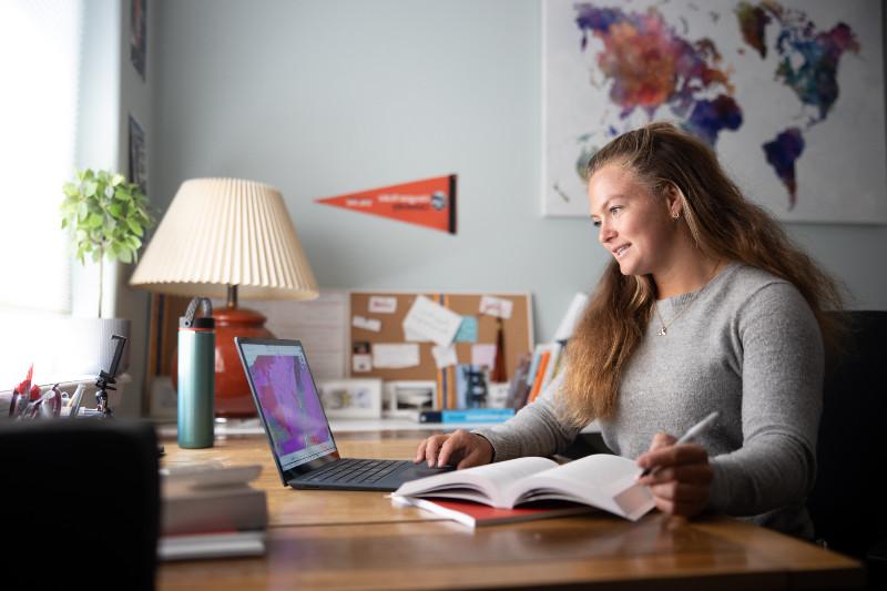 person at a laptop working from a textbook while looking at data on the laptop